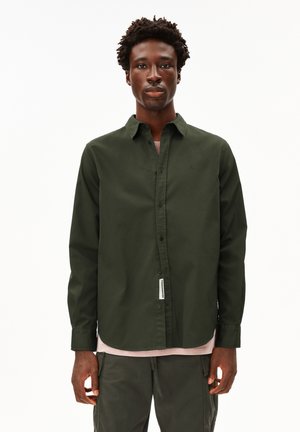 Donkergroene overhemd met kraag, lange mouwen en een subtiele merketiket aan de zoom; gedragen over een lichtroze shirt.