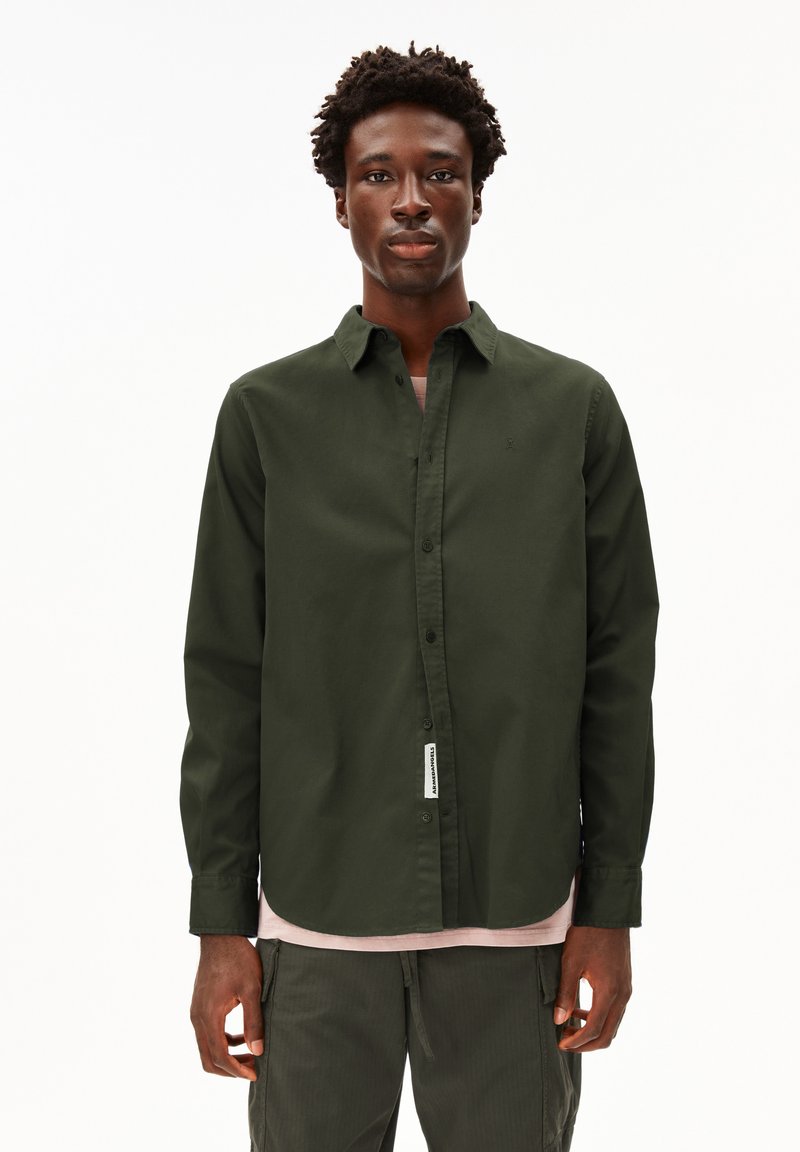 Dark green button-up shirt with a collar, long sleeves, and a subtle brand tag along the hem; worn over a light pink shirt.