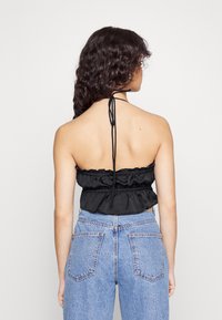 Top halter preto com bainha rendada, feito de tecido leve, combinado com jeans de cintura alta azul clara com bolsos traseiros.