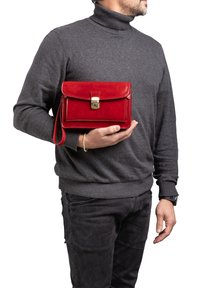 Rode leren handtas met een klep aan de voorkant en gouden hardware. De tas heeft een rits rondom en een polsband voor gemakkelijk vervoer.