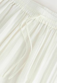 Ceinture élastique avec cordon sur tissu blanc léger, montrant une texture froncée et une coupe ample.