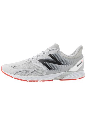 Lysegrå New Balance løbesko med sort logo, hvid og rød sål, mesh og ruskind øvre, og "BHANZO" branding på hælen.