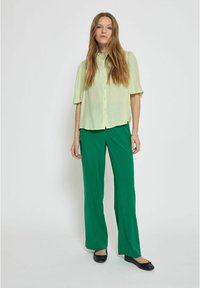 Camicetta verde chiaro a maniche corte con bottone, dalla vestibilità ampia, abbinata a pantaloni lunghi verdi e ballerine nere. Design semplice e traspirante.