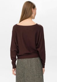 Brauner oversized Pullover mit weitem Ausschnitt, fallenden Schultern und geripptem Saum, kombiniert mit einem gemusterten grauen Rock.