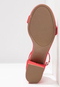 Vue de la semelle d'une sandale rouge avec un talon bloc et une bride à la cheville, montrant une semelle extérieure texturée pour l'adhérence et l'empreinte de la marque "Call It Spring".