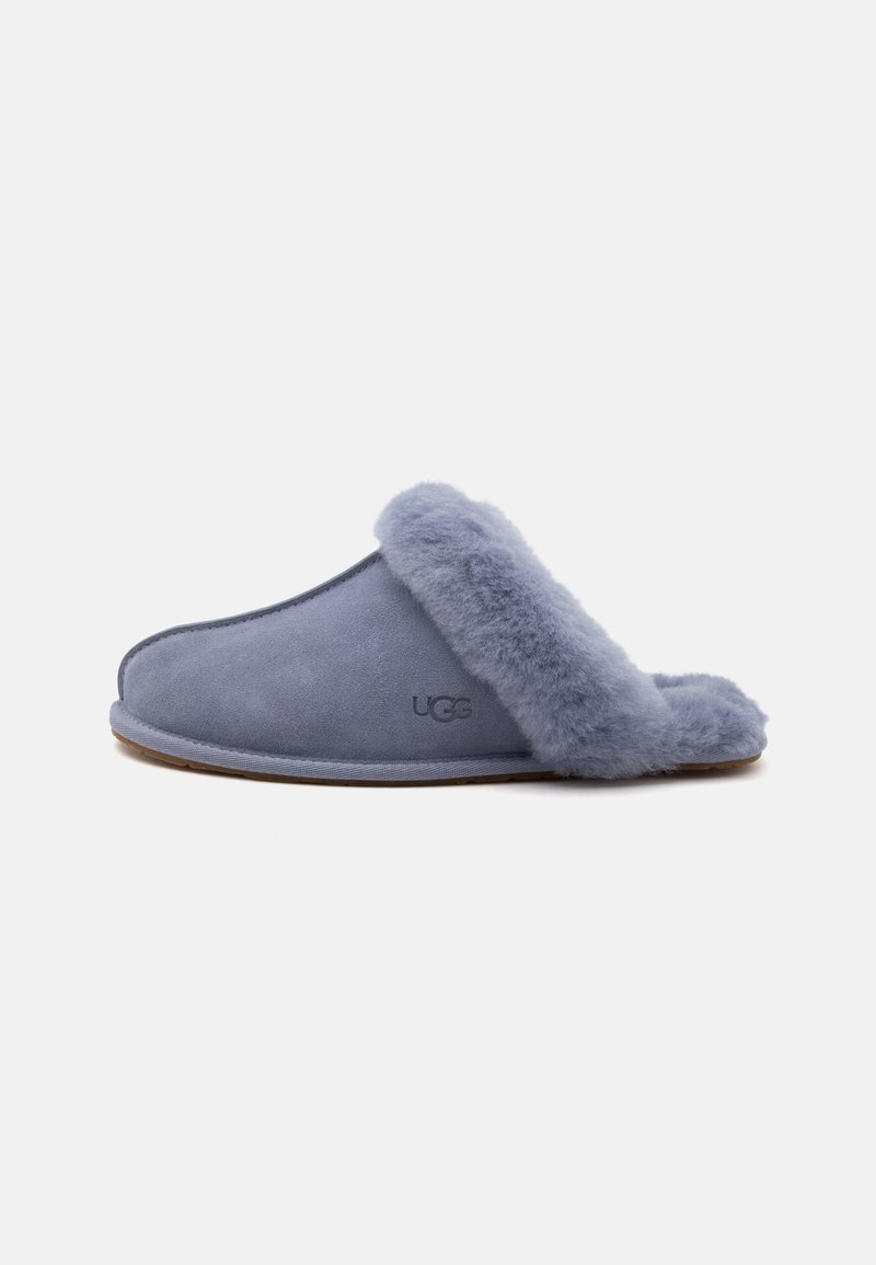 Απαλή γαλάζιο-γκρι παντόφλα τύπου slip-on με επένδυση και διακόσμηση από πλούσια γούνα, χαμηλό τακούνι και λογότυπο UGG στο πλάι.