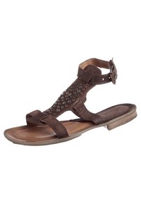 Brun lädersandal med flat sula, dekorativa metallnitar på ovandelen och ett justerbart ankelfäste med spänne.