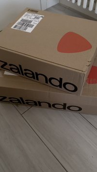 Kaks pruuni pappkarpi Zalando logoga, millest ühel on punane kolmnurkne disain. Ülal on nähtavad etikettide ribakoodid.
