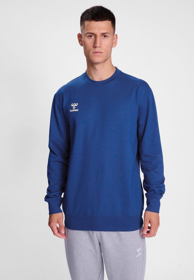 Blå långärmad sweatshirt i mjukt tyg, med rundad halsringning, ribbade ärmslut och en liten vit logotyp på vänster bröst.