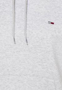 Sweat à capuche gris clair chiné avec cordons blancs et un petit logo rectangulaire rouge, blanc et noir sur la poitrine.