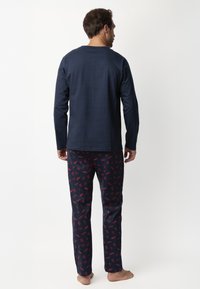 Top de manga larga azul marino con cuello redondo, combinado con pantalones de pijama estampados que presentan gráficos rojos, confeccionados en una suave mezcla de tejidos.