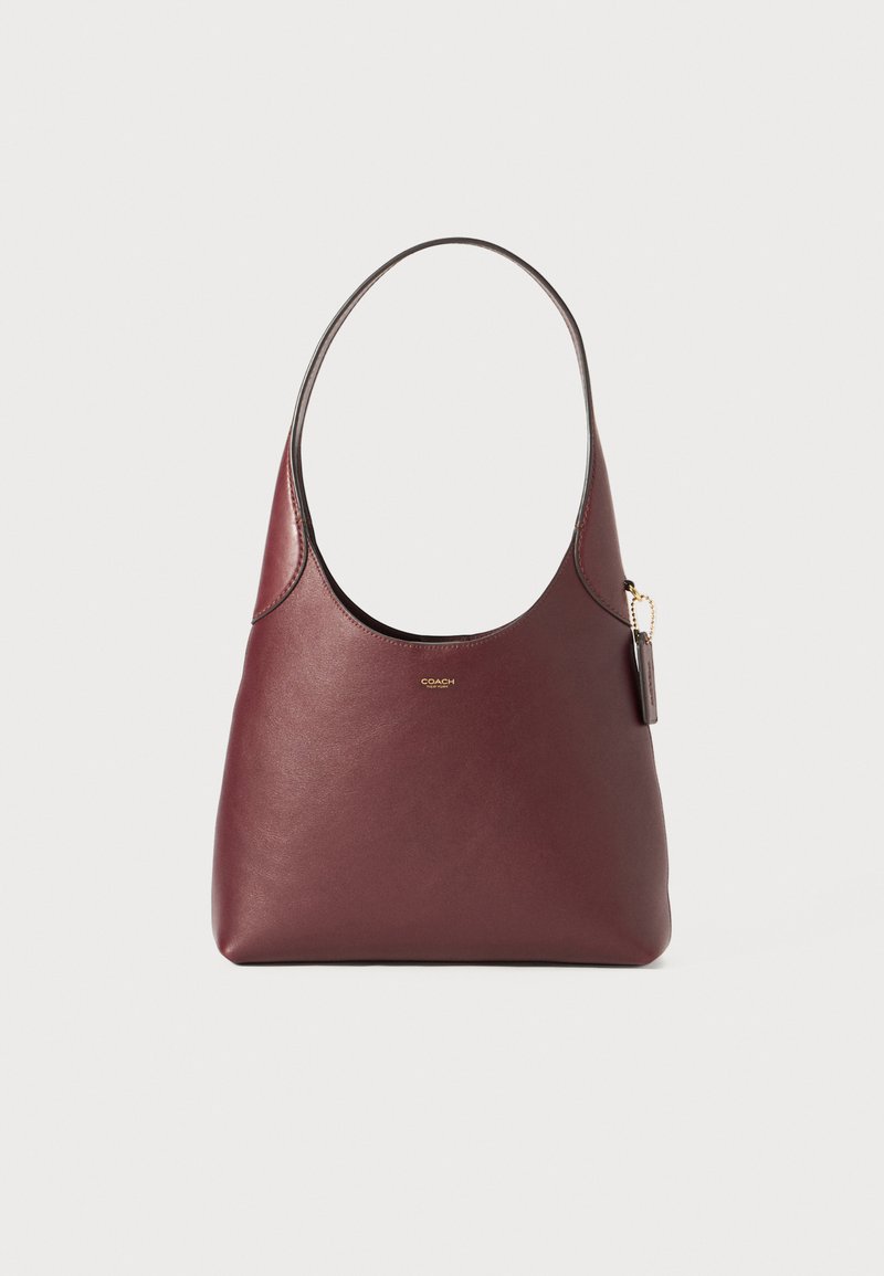 Burgundy leather hobo bag with a smooth texture, a wide opening, and a short handle. Features a gold logo and a detachable tag.
