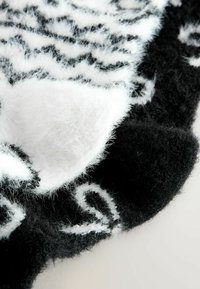 Fekete-fehér mintás takaró, bolyhos textúrával, hullámos fehér vonalakkal fekete anyagon és egy puha fehér díszítéssel.