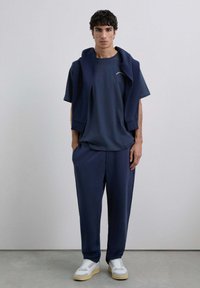 Conjunto a juego en azul marino que incluye una blusa de manga corta y pantalones ajustados, con un suéter caído sobre los hombros y zapatillas blancas.