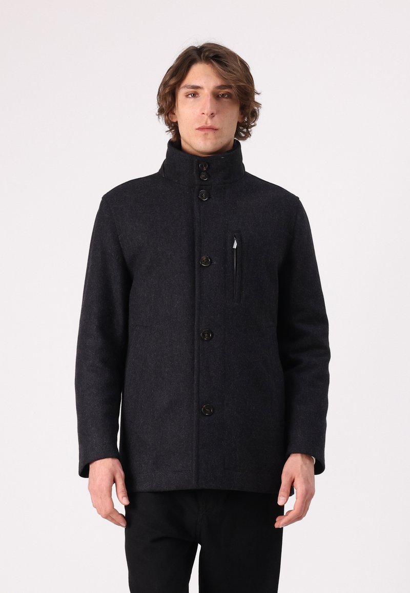 Dunkler Wollmischmantel mit hohem Kragen, vorderem Knopfverschluss, einer Brusttasche und taillierter Passform. Glatte Textur und minimalistisches Design.