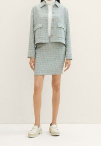 Giacca in tweed azzurro chiaro con due tasche frontali, chiusura con bottoni, abbinata a una gonna fitted coordinata. Portata con mocassini bianchi.