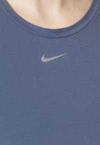 Granatowy sportowy top na ramiączkach o gładkiej fakturze, z małym srebrnym logo Nike na środku klatki piersiowej i okrągłym dekoltem.
