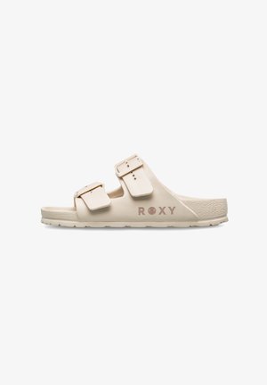 Beige slipper met twee verstelbare banden en een gestructureerde zool. Heeft een gegraveerd "ROXY" logo aan de zijkant. Gladde afwerking van het materiaal.