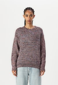 Strikkegenser i flerfarget garn med rund hals og lange ermer. Løs passform og teksturert stoff, kombinert med lyseblå jeans.