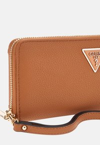 Tasche aus strukturiertem Leder mit goldenen Beschlägen, Reißverschluss und Logo-Platte. Verfügt über einen Handgelenktragegurt für einfaches Tragen.