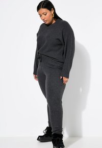 Dunkelgrauer Strickpullover mit rundem Halsausschnitt, kombiniert mit passenden, figurbetonten Hosen. Der Pullover hat einen Bindedetail in der Taille und gerippte Bündchen.