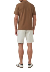 Brązowa koszula z krótkim rękawem o teksturowanej tkaninie, w połączeniu z jasnobeżowymi szortami i casualowymi białymi trampkami z czarnymi akcentami.