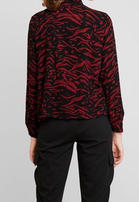 Blusa nera con stampa animale rossa, maniche lunghe, vestibilità ampia e polsini con bottoni. Abbinata a pantaloni cargo neri con tasche laterali.