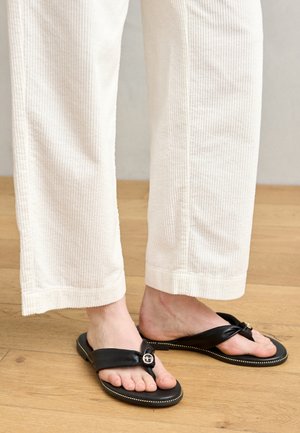 Juodų šlepečių su tvirtu padu ir plonomis juostelėmis, puoštų dekoratyvine sagtimi, derinamos su kreminių veliūrinių plačių kelnių.