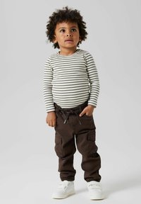 Stripete langermet skjorte i beige og brunt, kombinert med brune cargobukser med lommer, og hvite sko med borrelås.