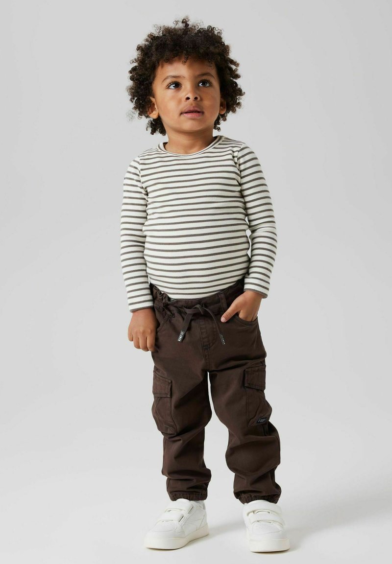 Stripete langermet skjorte i beige og brunt, kombinert med brune cargobukser med lommer, og hvite sko med borrelås.