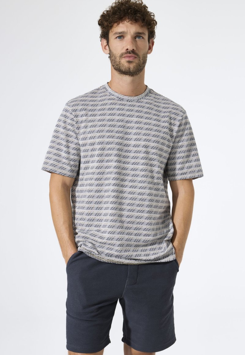 Kurzärmeliges T-Shirt mit Rundhalsausschnitt in Hellgrau mit dunkelblauen geometrischen Streifen. Kombiniert mit marineblauen Shorts aus strukturiertem Stoff.