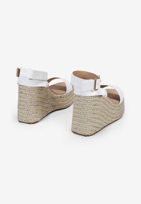 Sandalias de cuña blancas de cuero con correa ajustable en el tobillo, que presentan una suela de yute trenzado y una plantilla lisa color beige.