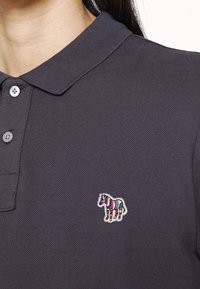 Gros plan d'un polo gris foncé avec deux boutons et un petit logo zèbre coloré brodé sur la poitrine.