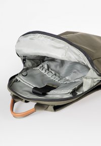 Zaino verde oliva con un esterno liscio, foderato internamente in grigio, con chiusura a zip e manico in pelle. Presenta tasche interne e cinghie.