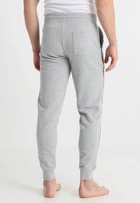 Pantalones de chándal de algodón gris con un ajuste ajustado, cintura elástica y franjas laterales. Cuenta con un bolsillo trasero y puños acanalados.
