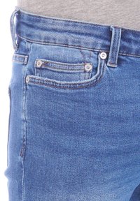 Jean en denim bleu avec un design classique à cinq poches, fermeture à bouton et coutures contrastantes, le tout avec une texture douce.