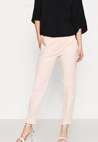 Pantalon rose clair en tissu doux, avec une coupe fuselée et des poches latérales. Associé à un haut noir et des talons blancs à lanières.