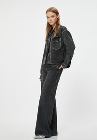 Svart denimjacka med vit sömnad, två bröstfickor, tillsammans med svarta vida jeans. Tyget har en strukturerad yta.