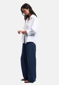 Chemise blanche à manches retroussées, associée à un pantalon large en tissu lisse de couleur marine. Design simple, coupe décontractée.
