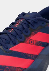 Marineblaue und rote Sportschuh mit marinefarbenen Schnürsenkeln, roten Streifen und floralem Muster am oberen Teil in der Nähe der Schnürsenkel.