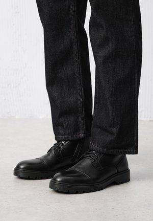 Czarne skórzane botki z okrągłym przodem i teksturowaną podeszwą. Sznurowane z przodu. W połączeniu z ciemnoniebieskimi dżinsami o prostym kroju.