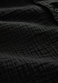 Nærbillede af struktureret sort stof med synligt vævemønster og en enkelt sort knap øverst til højre.