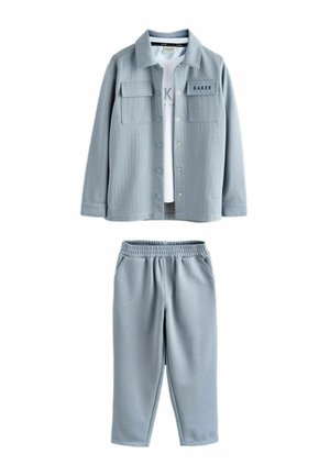 Lyseblåt todelt sæt med knapoplukket jakke med forlommer og bukser med elastik i taljen, lagdelt over en hvid trykt skjorte.