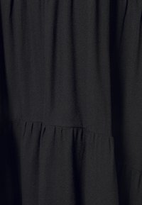 Svart klänning med lätt, texturerad tyg. Designen inkluderar veckad detalj och en lager-på-lager siluet.