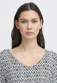 Haut à motif noir et blanc avec un décolleté en V. Le tissu a une texture douce, présentant un motif géométrique répété.