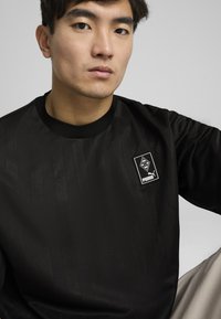 Sort atletisk sweatshirt med et tekstureret mønster, rund halsudskæring og et logopatch med en diamantform på brystet.