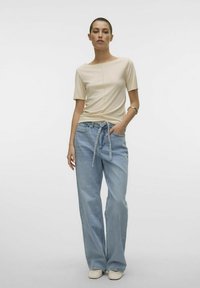 Beige kortærmet top med bådudskæring og midtersøm, kombineret med lyseblå vide jeans med knyttet talje og sidelommer.