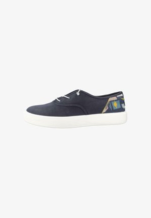 Zapatilla baja de lona azul marino con suela blanca, cordones blancos y talón estampado con formas abstractas y un diseño de sol amarillo.