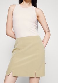 Débardeur côtelé rose clair associé à une mini-jupe kaki avec des fentes sur les côtés. Tissu lisse, design ajusté, style minimaliste.
