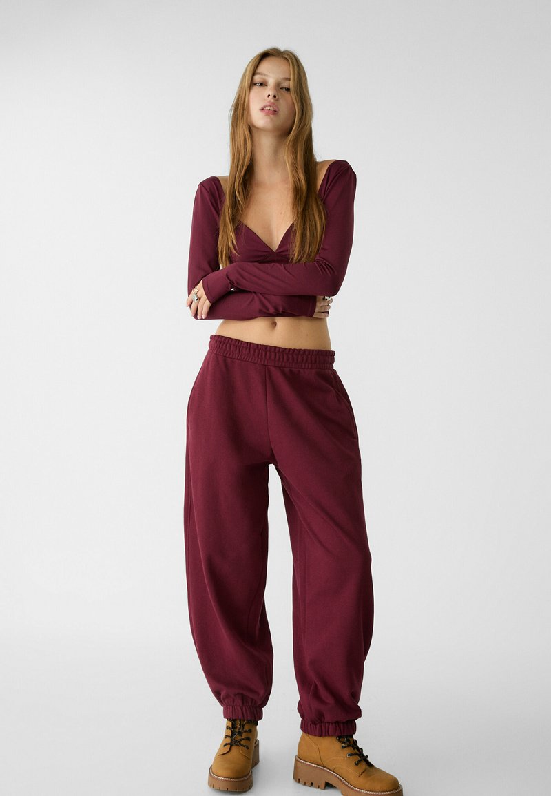 Maglia bordeaux a maniche lunghe con scollatura a V e vestibilità aderente, abbinata a jogger bordeaux larghi e stivali color cammello con lacci e suola spessa.